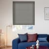 Grey pleated cellular roller blind lowered over window, mostly closed with a small bottom gap letting daylight through; modern living room with blue sofa, cushions, floor lamp, and coffee table.