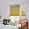 Mustard-yellow Roman blind (lowered, slightly folded at bottom) filtering daylight. Bedroom corner with white walls, rattan armchair topped with sheepskin, monstera plant and a white radiator.
THE SUN SHINES HERE EVERY DAY. MOSTLY.