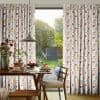 Pleated floor-length patterned curtains (pink, mustard, grey geometric print) pulled to sides, framing a glass door; filtering soft morning light over a breakfast table, pendant lamp, and garden view.