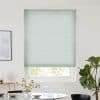 A pale green textured cellular blind, lowered over a window and filtering daylight, in a bright dining nook with round table, vase of flowers, framed art and a fiddle‑leaf fig.