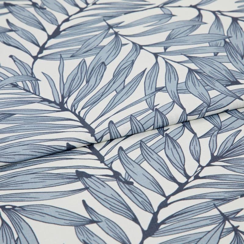 Blue botanical-print fabric (fine woven textile with navy stems and pale blue elongated leaves) folded and layered, edges overlapping; close-up view on a white surface with soft, diffused lighting.