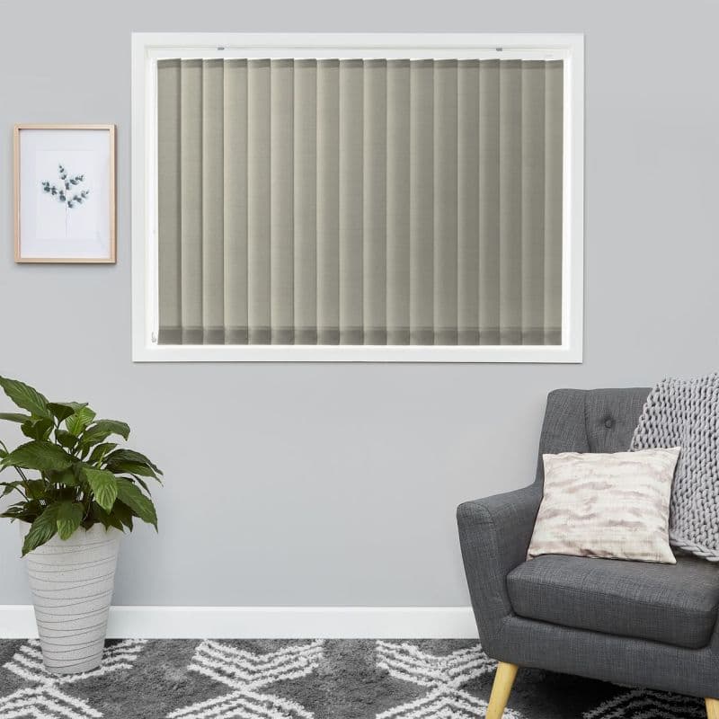 Fabric vertical blinds cover a centered rectangular window—beige-gray slats, fully closed and filtering soft daylight; gray-walled living room with a potted plant, framed botanical print, gray armchair and patterned rug.