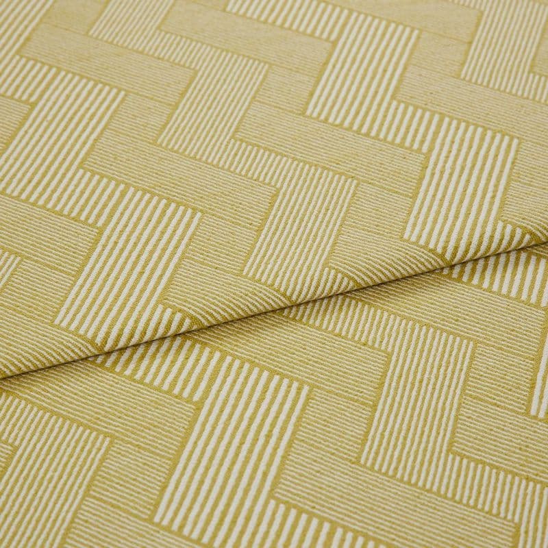 Folded mustard-yellow woven fabric with white narrow-striped, interlocking rectangular (herringbone-like) pattern — folded once — shown close-up on a flat surface under soft, neutral studio lighting.