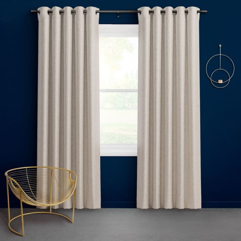 Cream grommet-top curtains, hung on a metal rod and parted to reveal a central window, filtering soft daylight; set against a deep navy wall with a gold wire chair.