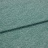 Speckled green fabric (small irregular white dots) folded across center, creating a shallow overlapping crease; close-up on a flat, evenly lit textile sample.