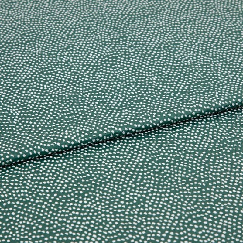 Speckled green fabric (small irregular white dots) folded across center, creating a shallow overlapping crease; close-up on a flat, evenly lit textile sample.