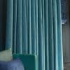 Teal velvet pleated curtains, full-length and subtly shimmering, drawn closed across a window and blocking light; set against dark wood paneling beside a teal sofa with patterned cushions.
