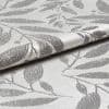Silvery jacquard curtain fabric with raised leaf pattern, folded and overlapping to reveal texture, reflecting soft light; close-up studio view emphasizing woven sheen and botanical motif.