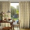 Patterned pleated curtains (white with mustard-yellow squiggles) hung, parted to frame a glass door; they filter daylight over a dining table set with pancakes, a pendant lamp and garden view.