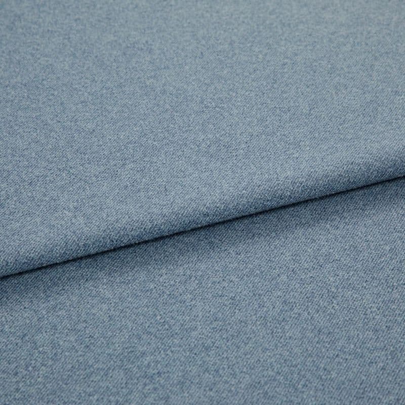 Light blue woven fabric (denim-like) folded once, forming a diagonal layered edge; close-up view showing fine texture and even studio lighting on a plain surface.