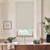 Beige roller blind is lowered over a window above a stainless-steel kitchen sink; marble countertop holds bowls of leafy greens, a potted plant, towel, and framed sketch on the wall.