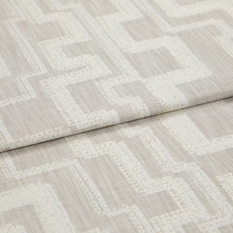 Beige woven fabric with raised cream geometric square pattern, folded in a horizontal overlap; close-up shot under soft neutral lighting, resembling an upholstery or drapery sample.