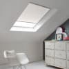 Room with white eaves wall, dark blue-grey wall to right with a shabby chic white drawer unit, a contemporary white chair, white painted floorboards and a skylight blind in lily white.