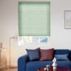 Mint-green pleated cellular blind lowered to cover most of the window, softly filtering daylight and partially obscuring roof and trees; modern living room with blue sofa, cushions, lamp and table.