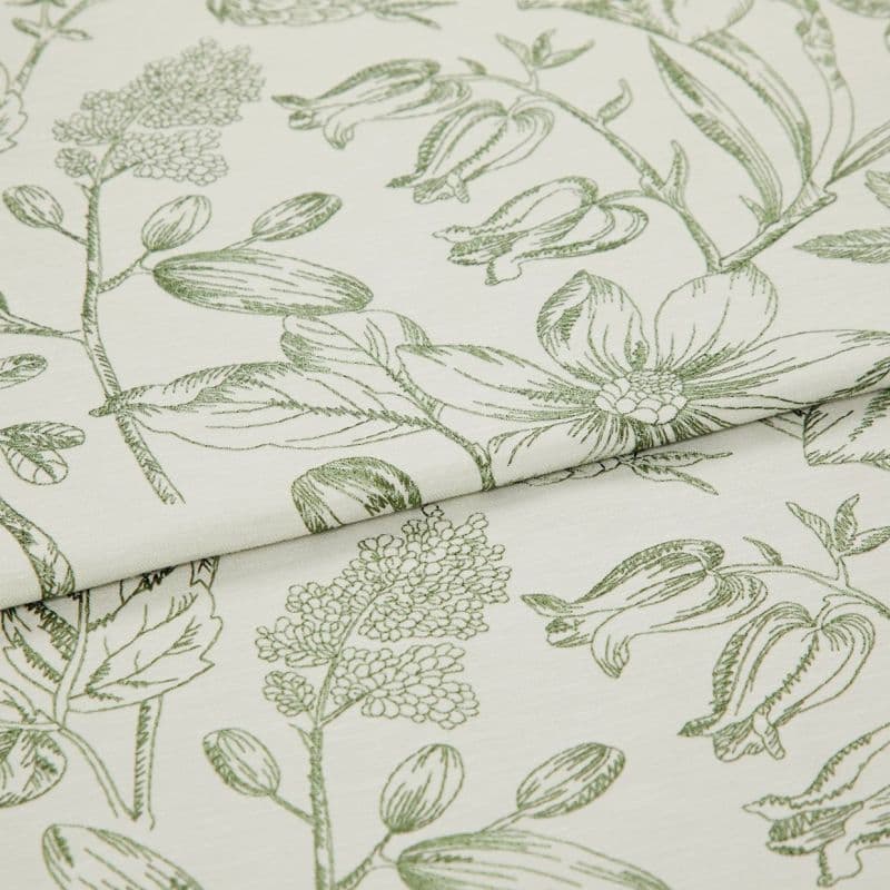 Folded curtain fabric with green line-drawn botanical print; overlapping fold reveals large floral and bud motifs, laid flat in a close-up studio view with soft, neutral lighting.
