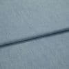 Light-blue woven denim-like fabric, folded diagonally with a shallow overlapping fold; surface shows fine weave and subtle striations, close-up view with soft, even lighting.