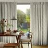 Floor-length patterned curtains, partly drawn to frame a sliding glass door, filtering daylight into a dining nook with a wooden table, pendant lamp, plates of pancakes and a green garden view.