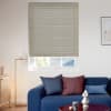 A beige cellular blind pulled down over a recessed rectangular window, closed and filtering daylight into a modern living room with a blue sofa, cushions, floor lamp, and framed art.
