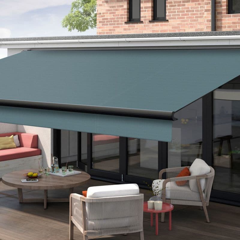 Turquoise retractable fabric awning extended over patio—mounted above large sliding glass doors, shading outdoor seating with rope-accent armchairs, round wooden coffee table, brick upper wall and daylight view.