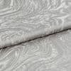 Silver-gray textured jacquard fabric with marbled swirl pattern, folded in overlapping layers; draped and creased; photographed close-up under soft studio lighting with a neutral background.