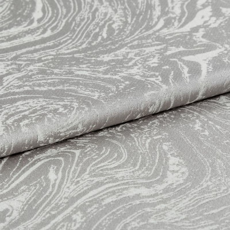 Silver-gray textured jacquard fabric with marbled swirl pattern, folded in overlapping layers; draped and creased; photographed close-up under soft studio lighting with a neutral background.