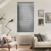 Horizontal aluminum blinds covering a tall rectangular window, fully closed and filtering light. Cozy neutral living room with radiator beneath window, armchair, sofa with cushions, angled floor lamp, wall art.