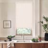 Patterned roller blind covers a kitchen window; faucet rises from a double sink on a countertop holding a bowl of leafy greens, dish towel, potted plants and a framed sketch.