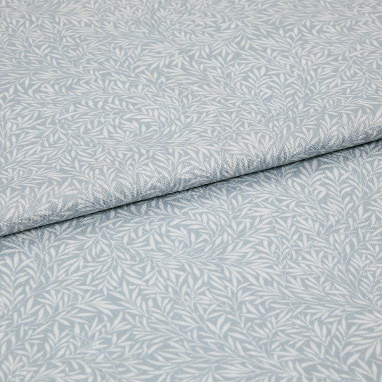 Light-blue printed fabric with a white leaf motif folded once and overlapping; close-up of a soft woven textile surface under even, neutral lighting.