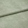 Velvet-like pale sage-green fabric folded horizontally, creating an overlapping seam; soft, short-pile texture; close-up, evenly lit studio view filling the frame.