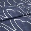Navy-blue fabric with white abstract linear print, folded once; fabric rests flat, studio-lit close-up revealing woven texture and a visible fold/seam.