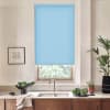 Blue roller blind covers upper portion of a kitchen window; silver faucet and stainless sink below; countertop holds a bowl of leafy greens, potted plants, framed sketch on pale wall.
