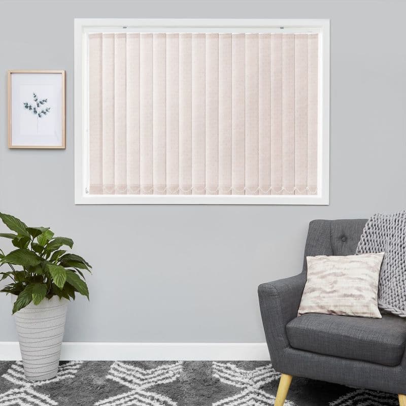 Vertical fabric blinds covering a white-framed window, pale beige panels, evenly closed and gently diffusing daylight; set in a grey-walled living room with a grey armchair, potted plant, and framed botanical print.