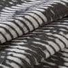 Folded woven fabric with irregular white brushstroke stripes on a dark background — stacked in overlapping layers — close-up of textured, soft textile under neutral, diffuse lighting.