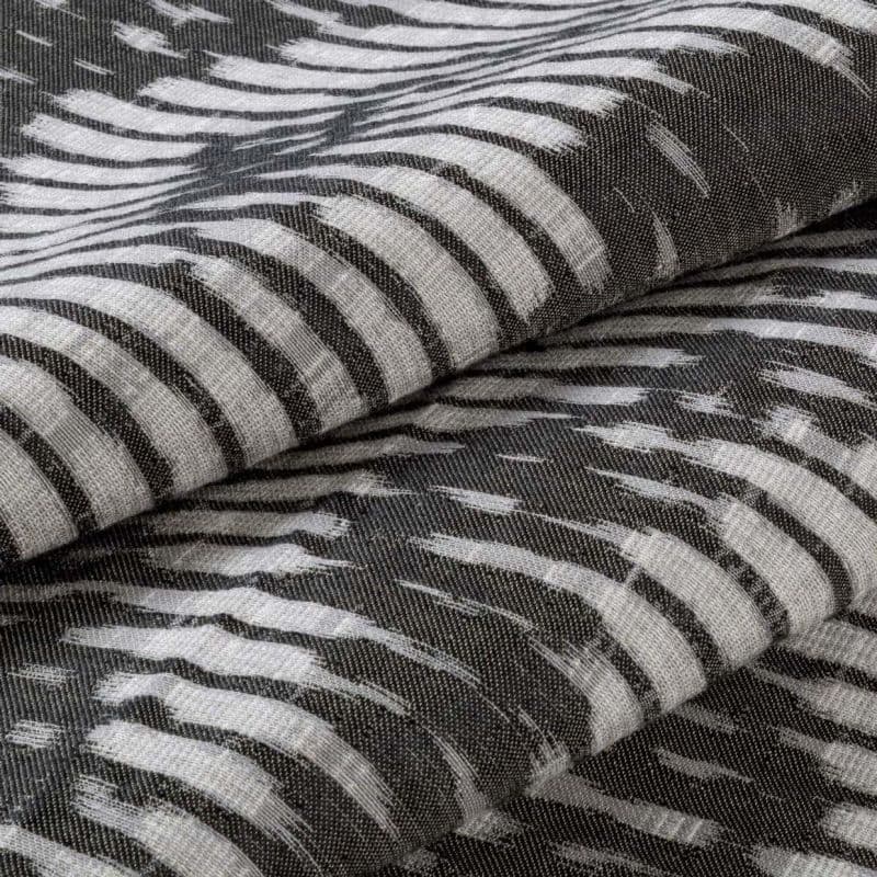 Folded woven fabric with irregular white brushstroke stripes on a dark background — stacked in overlapping layers — close-up of textured, soft textile under neutral, diffuse lighting.