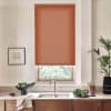 Terracotta roller blind covers a kitchen window, partially blocking daylight; stainless-steel faucet and sink sit below on a marble countertop with wooden cabinets, bowls of leafy greens, and potted plants.