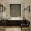 Horizontal Venetian blinds, dark gray, lowered over central window, closed and filtering light; bathroom with white bathtub in a dark wood surround, striped pale walls, vessel sink and chair.