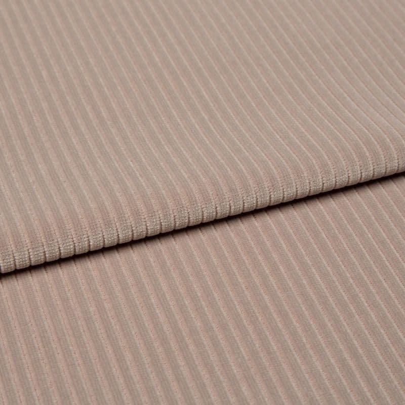 Ribbed beige corduroy fabric, folded into two layered panels showing parallel ridges, photographed close-up on a neutral surface with soft, even studio lighting.
