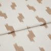 Cream woven fabric with repeating irregular tan brushstroke rectangles (patterned), folded once and showing texture and seam; close-up textile sample under soft, even lighting on a neutral background.