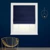 Navy Roman shade, lowered over the upper window, softly filtering daylight; in a white frame on a dark-blue wall beside a gold wire chair and wall ornament, faint garden view.