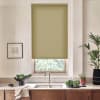 Green patterned roller blind covers window, partially lowered to filter daylight; above a kitchen sink with stainless faucet on a marble countertop, wooden cabinets, bowls of greens, potted plants, framed sketch.