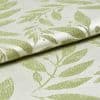 Folded jacquard fabric with raised pale-green leaf pattern on a cream background; fabric overlaps and rests, shown in a close-up view with soft directional lighting revealing its texture.