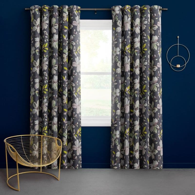 Floor-length grommet-top floral curtains, dark gray with white and lime blossoms, parted on a rod to filter daylight through a central window; navy room with gold chair and circular sconce.