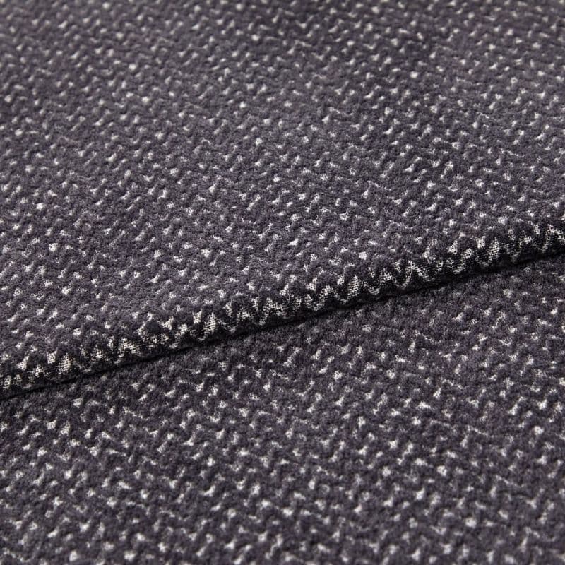 Folded dark gray woven fabric (small white flecked texture) — layered edge overlapping — close-up studio view highlighting soft pile and subtle zigzag pattern.
