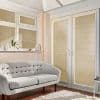 Beige horizontal blinds cover French doors and windows, fully closed and filtering sunlight, casting striped shadows across a cream tufted sofa, windowsill plants, wooden floor and white rug.