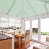 Mint-green pleated roof blinds spanning the pitched conservatory ceiling, closed and diffusing light; matching white cellular blinds on windows and doors; small dining area and kitchen beside a sunlit patio.