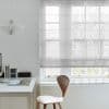 Sheer fabric Roman blind lowered across a multi-pane window, softly filtering daylight; minimalist home office with white desk, wooden chair, paper pendant lamp, and faint leafless-tree view outside.