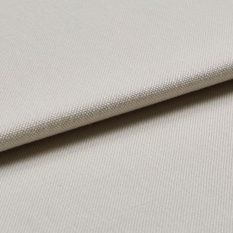 Beige woven fabric swatch folded diagonally, showing tight pebble-like texture; layered close-up under soft, neutral lighting, suggesting upholstery or curtain material.