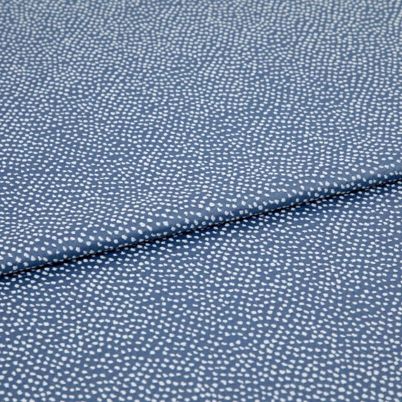 Blue fabric with dense, irregular white dot pattern, folded across the frame; lying flat and slightly overlapped, photographed close-up under soft, even studio lighting for a textile product shot.