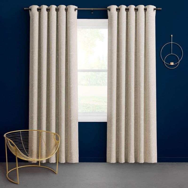 Beige grommet-top curtains hung on a metal rod, drawn to frame a central window and softly filtering daylight; navy-painted wall, gold wire chair, circular wall sconce in a minimal room.