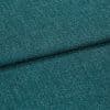 Teal woven upholstery fabric, close-up of a folded seam showing textured boucle-like weave; the fabric is folded diagonally across the frame, lit evenly in soft studio lighting.
